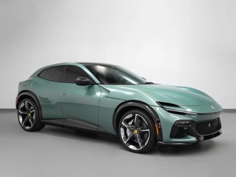 A metallic green Ferrari Purosangue SUV is parked in a plain indoor setting, viewed from the front left angle.