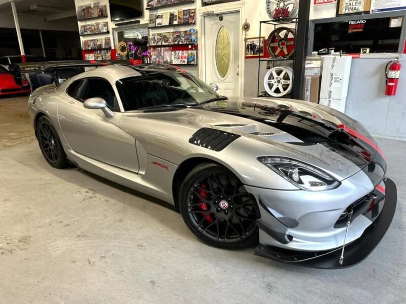 Dodge Viper Silver with black accents and front mixture inside a garage or workshop - a major example of one of the best manual transmission cars. Car and souvenirs are displayed on the walls.