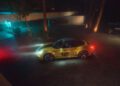 A limited edition yellow Porsche 911 Spirit 70 with "70" on the door is parked on a stone driveway at night, illuminated by headlights and nearby neon lighting.