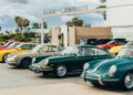 A row of vintage and classic cars, including Porsche models, parked in front of a building with a "Pacific Amphitheatre" sign on a cloudy day during the 2025 Air|Water Event.