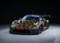 A stunning Porsche 911 GT3 R with a gold and black swirled pattern design is captured from the front against a dark background, evoking the thrill of a race at Spa.