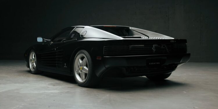 A sleek black Ferrari 512 TR with a low-profile design and angular lines rests on a smooth gray surface in a dimly lit setting, exuding the curated elegance once admired by icons like Michael Jordan.