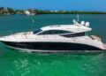 A white and black luxury motor yacht cruises on calm green water near waterfront homes under a clear blue sky, offering an unparalleled maritime experience for those seeking the finest luxury yachts.