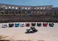 The Trailblazers Tour showcases a collection of nine sports cars, including the Rimac Nevera, with open gullwing doors arranged in a semicircle inside an ancient amphitheater.