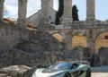A sleek green Rimac Nevera sports car is parked in front of an ancient stone amphitheater with large arches, basking under a clear blue sky, as if on a Trailblazers Tour.