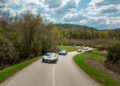 Several sports cars, including sleek Rimac Neveras, drive on a winding rural road surrounded by trees under a partly cloudy sky as part of the Trailblazers Tour.