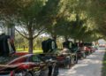 A line of Rimac Neveras with open gullwing doors is parked on a gravel path under tall trees, ready to lead the Trailblazers Tour.