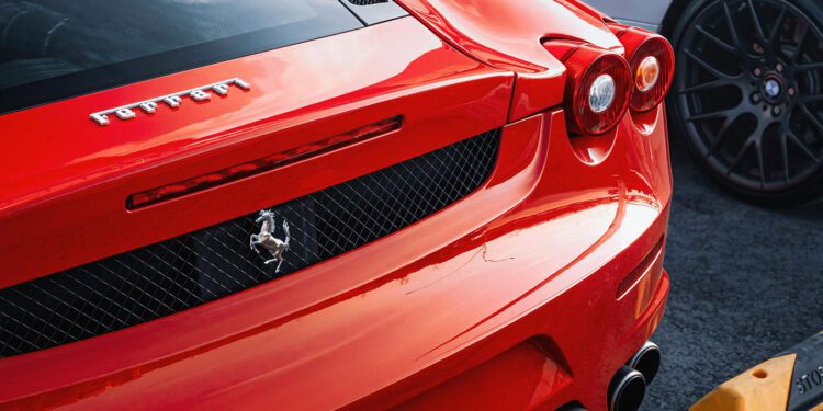 Rear view of a red Ferrari parked next to another car, showcasing its logo, taillights, and exhaust—a perfect candidate for exotic car insurance.