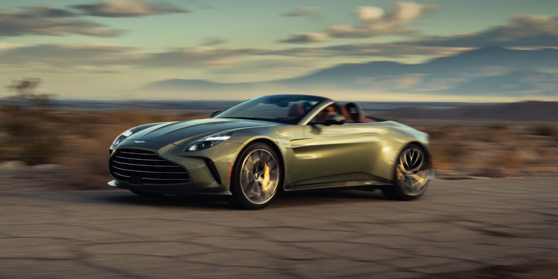 A green convertible sports car driving on a deserted road through a scenic, arid landscape with mountains in the background.