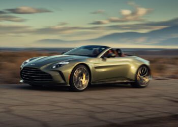 A green convertible sports car driving on a deserted road through a scenic, arid landscape with mountains in the background.