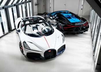 Two luxury sports cars, including a stunning Bugatti W16 Mistral with blue accents, are parked side by side in a well-lit, modern garage after a recent Bugatti delivery from O'Gara Coach.
