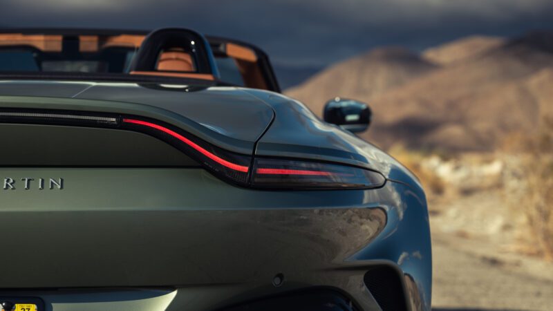 Close-up of the rear end of a green convertible sports car with a distinctive LED tail light, desert mountains blurred in the background.