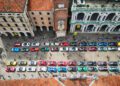 Aerial view of the Cavalcade Siviglia in Andalusia, where rows of colorful Ferrari sports cars are parked in a city square surrounded by historic buildings, as crowds stroll among the stunning vehicles.