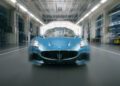 A blue Maserati GranTurismo is parked in a brightly lit automotive factory, viewed from the front with a slight motion blur effect around the edges.
