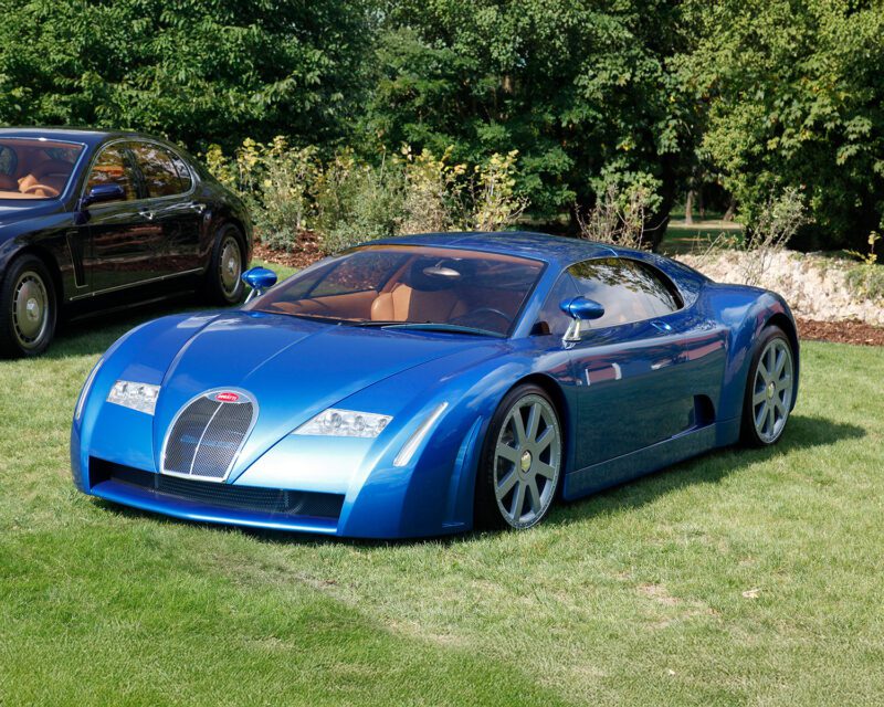 A blue Bugatti concept sports car parked on grass, with another car and greenery visible in the background.