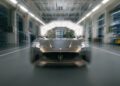 A Maserati GranTurismo sports car is photographed head-on inside a brightly lit industrial facility, with motion blur suggesting movement toward the camera.