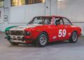 Red, white, and green vintage racing car with number 59, parked indoors in a warehouse with white walls and large windows; part of the RM Sotheby’s Quadrifoglio Collection Monterey 2025.