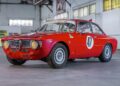 A red classic Alfa Romeo race car with the number 47 on the door is parked indoors in a spacious, industrial-style garage, part of the prestigious RM Sotheby’s Quadrifoglio Collection Monterey 2025.