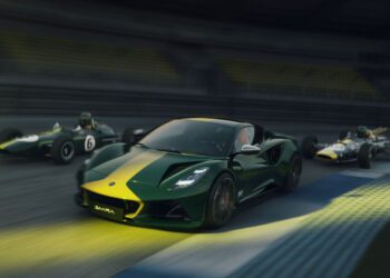 A modern green and yellow Lotus Emira Jim Clark Edition sports car races on a track alongside two vintage race cars, all moving at high speed with blurred backgrounds.