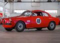 A red vintage race car with the number 48 on the door is parked indoors in a spacious garage, part of the RM Sotheby’s Quadrifoglio Collection, with other classic cars seen in the background.