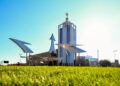 A modern building in Modena with a glass tower and Maserati logo stands behind metallic bird sculptures on a grassy lawn under a clear blue sky, reflecting the spirit of the GranTurismo.