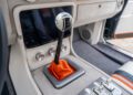 Close-up of a car's manual gear shift with an orange boot, white knob, and nearby control buttons inside a modern vehicle interior—reminiscent of the power found in a 1,000-HP Hellephant-powered 1969 Charger.