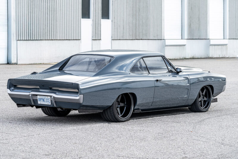 A gray 1969 Charger muscle car with black wheels is parked on a paved surface in front of an industrial building, hinting at a possible Hellephant 1,000-HP engine under the hood.