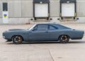 Side view of a gray 1969 Charger muscle car with black wheels, featuring a powerful Hellephant engine, parked in front of a warehouse loading dock.