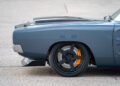 Close-up of the rear quarter panel of a gray muscle car, inspired by the legendary 1,000-HP Hellephant-powered 1969 Charger, featuring large black wheels with orange brake calipers and "Hellcat" text on the hood scoop.
