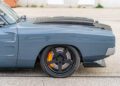 Close-up side view of a gray 1969 Charger’s front wheel and fender, featuring a black hood with “HELLAPHANT” text and visible orange brake calipers, hinting at its powerful Hellephant 1,000-HP engine.