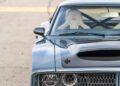 Close-up of the front left side of a silver 1969 Charger muscle car, featuring a hood scoop, headlight, grille, and part of a white racing seat—hinting at the power of its Hellephant 1,000-HP engine.
