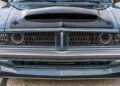 Close-up view of the front end of a 1969 Charger with a matte black hood scoop and detailed grille, parked on pavement—this muscle car packs the power of a Hellephant 1,000-HP engine under its iconic hood.