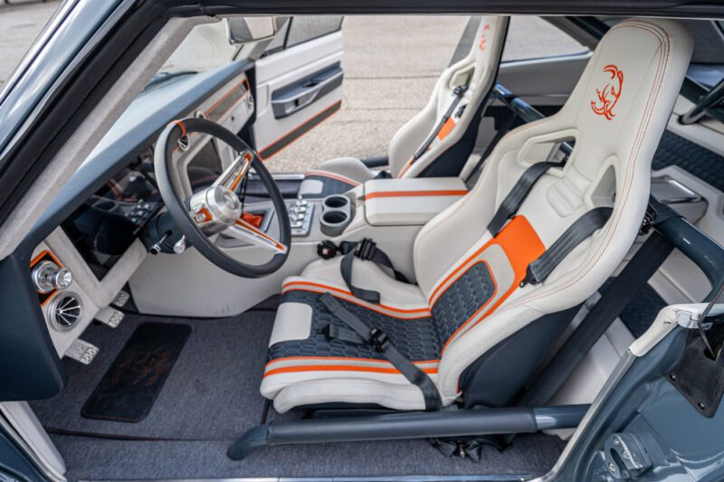 Interior of a modernized 1969 Charger featuring white and orange bucket seats with harnesses, a custom steering wheel, roll cage, and a center console with cup holders—built to match the thrill of its 1,000-HP Hellephant engine.