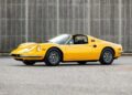 A yellow vintage Ferrari Dino 246 GTS sports car is parked on an empty street in front of a gray concrete wall, showcasing the timeless appeal of classic Ferrari Dino cars.