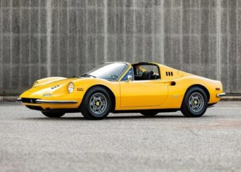 A yellow vintage Ferrari Dino 246 GTS sports car is parked on an empty street in front of a gray concrete wall, showcasing the timeless appeal of classic Ferrari Dino cars.