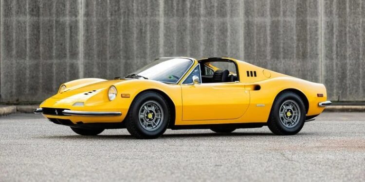 A yellow vintage Ferrari Dino 246 GTS sports car is parked on an empty street in front of a gray concrete wall, showcasing the timeless appeal of classic Ferrari Dino cars.
