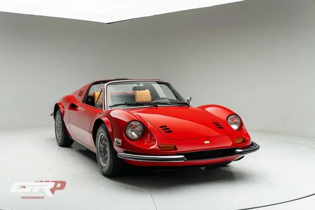A classic red Ferrari Dino sports car with a black targa top is parked in a white studio setting facing slightly left.
