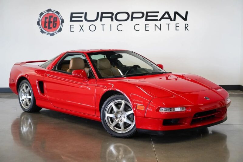 A red two-door sports car with tan interior, one of the best 2000s cars, is parked indoors in front of a wall displaying the European Exotic Center logo.