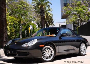 A black Porsche 911 convertible, one of the best 2000s cars, is parked on a sunny street lined with palm trees and modern buildings. A phone number for cars for sale appears at the bottom right of the image.