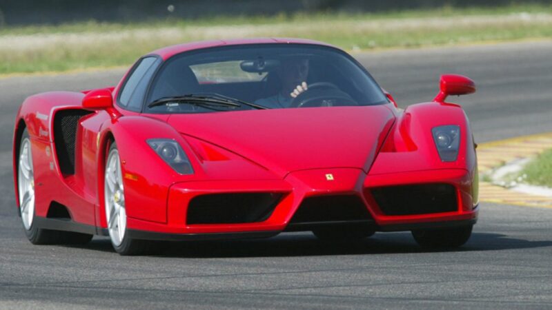 A red Ferrari Enzo sports car, inspired by the 10 Enzo Derivates That Only REAL Ferrari Fans Know About, speeds along a racetrack with a driver behind the wheel.
