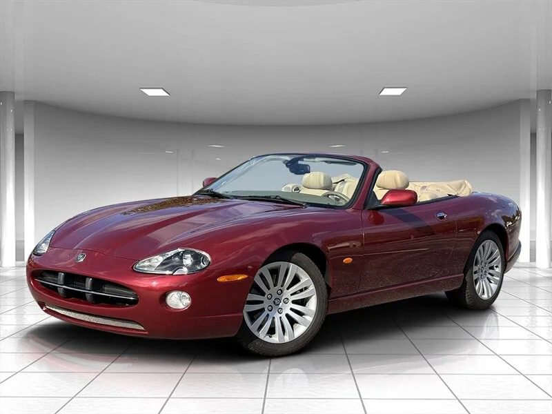 A stunning maroon convertible sports car with a beige interior, one of the best 2000s cars, is parked indoors on a tiled floor under ceiling lights.