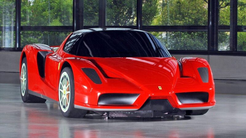 A red Ferrari sports car is parked indoors on a smooth floor, with large windows and greenery visible in the background—one of those 10 Enzo Derivates That Only REAL Ferrari Fans Know About.