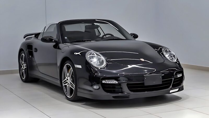 A black Porsche convertible sports car, considered among the best used cars for 100000, is parked indoors on a light-colored tiled floor against a plain gray wall.