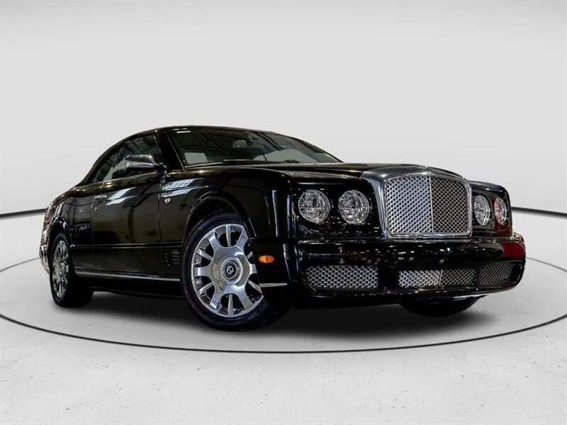 A black luxury coupe, one of the best 2000s cars, is parked in a well-lit showroom with a white background, viewed from the front left angle.