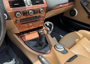 Interior of a car featuring tan leather seats, wood trim dashboard, manual gear shift, and central control buttons—a great option for those seeking the best manual transmission experience among cars for sale.