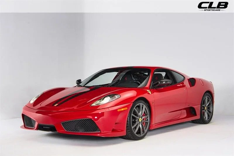 A red Ferrari sports car with black racing stripes is parked in a white studio setting, viewed from the front left side. Showcasing one of the best 2000s cars, the CLB Sports Cars logo is visible in the top right corner.