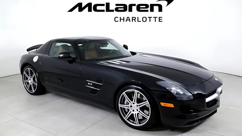 A black Mercedes-Benz SLS AMG coupe is parked indoors under a McLaren Charlotte sign, showcasing one of the best supercars under $200k now for sale.