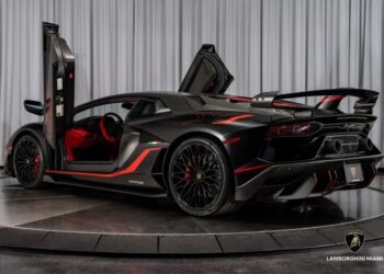 A matte black Lamborghini with red accents and scissor doors open is displayed on a rotating platform in a showroom, showcasing this luxury car as the ultimate exotic car experience.