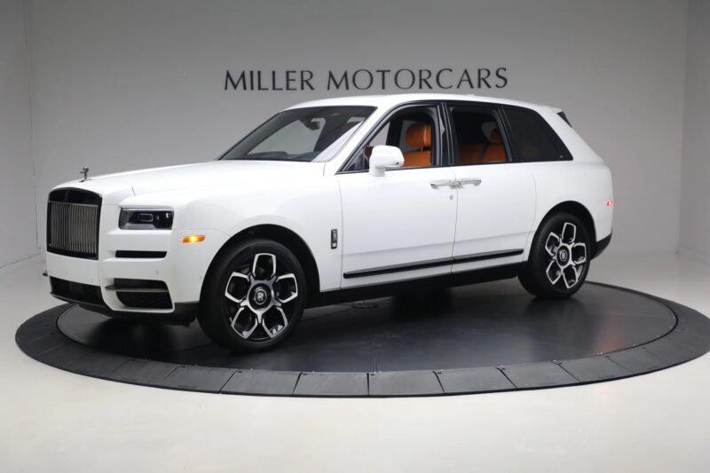 A white Rolls-Royce Cullinan, the pinnacle of luxury SUVs, is displayed in a showroom with "Miller Motorcars" on the wall behind it.