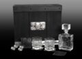 A whiskey decanter set with a decanter, two glasses, four metal dice, two coasters, and a sleek black box—each engraved—displayed against a gradient background. A crown jewel for collectors, much like the 2023 Dodge Challenger SRT Demon 170.
